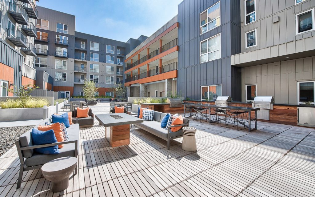Outdoor courtyard with lounge seating and tables, a fire table, grilling stations and a high-top dining table with bar stools.