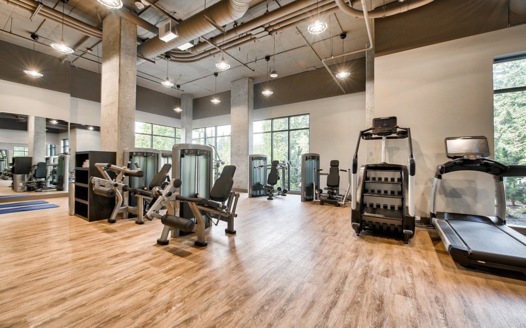 Fitness center with wood flooring, mirrored walls, exposed pipe ceiling, and weight machines, branches and treadmills.