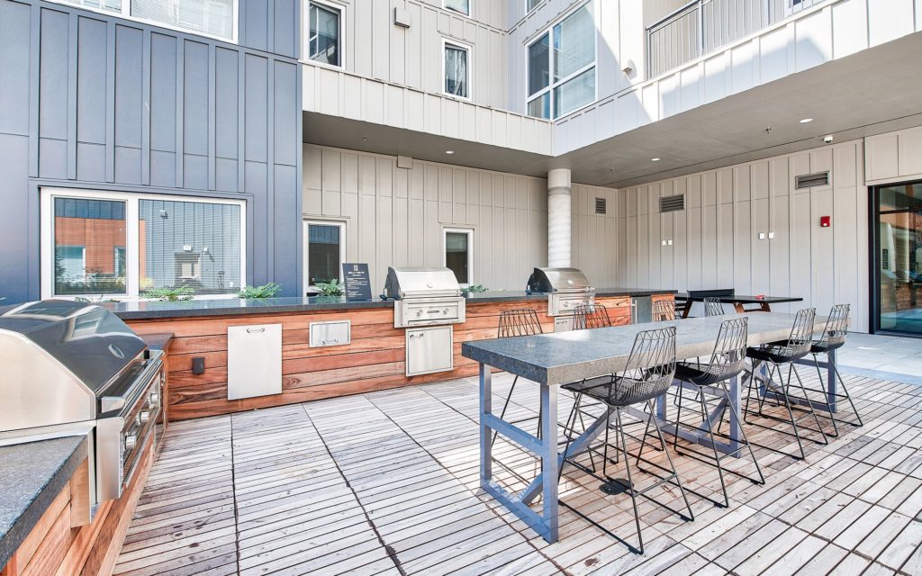 Courtyard close up featuring a pink pong table adjacent to three built-in grilling stations with counter prep space and a high-top dining table with bar stools.