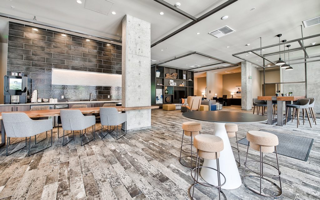 Clubhouse interior with lounge seating with TV, dining tables, a kitchen area, and computer stations.