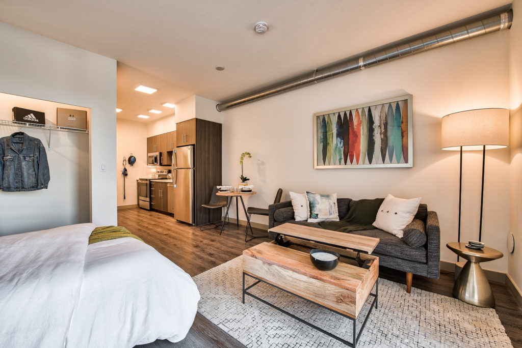 Alternate view of Furnished apartment living room with wood flooring, and large floor-to-ceiling windows with egress. Bed