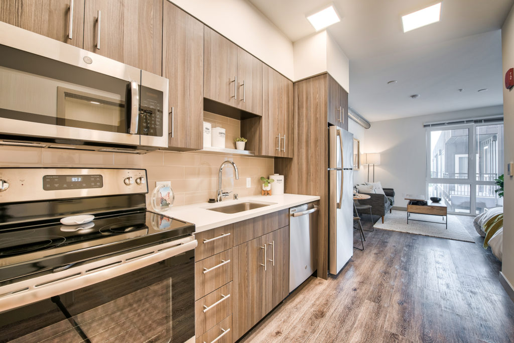 Alternate view of One-wall style kitchen with wood flooring, light countertops, and stainless-steel appliances including a top freezer style refrigerator, dishwasher, single basin undercounted sink, microwave, and over and stove combo.
